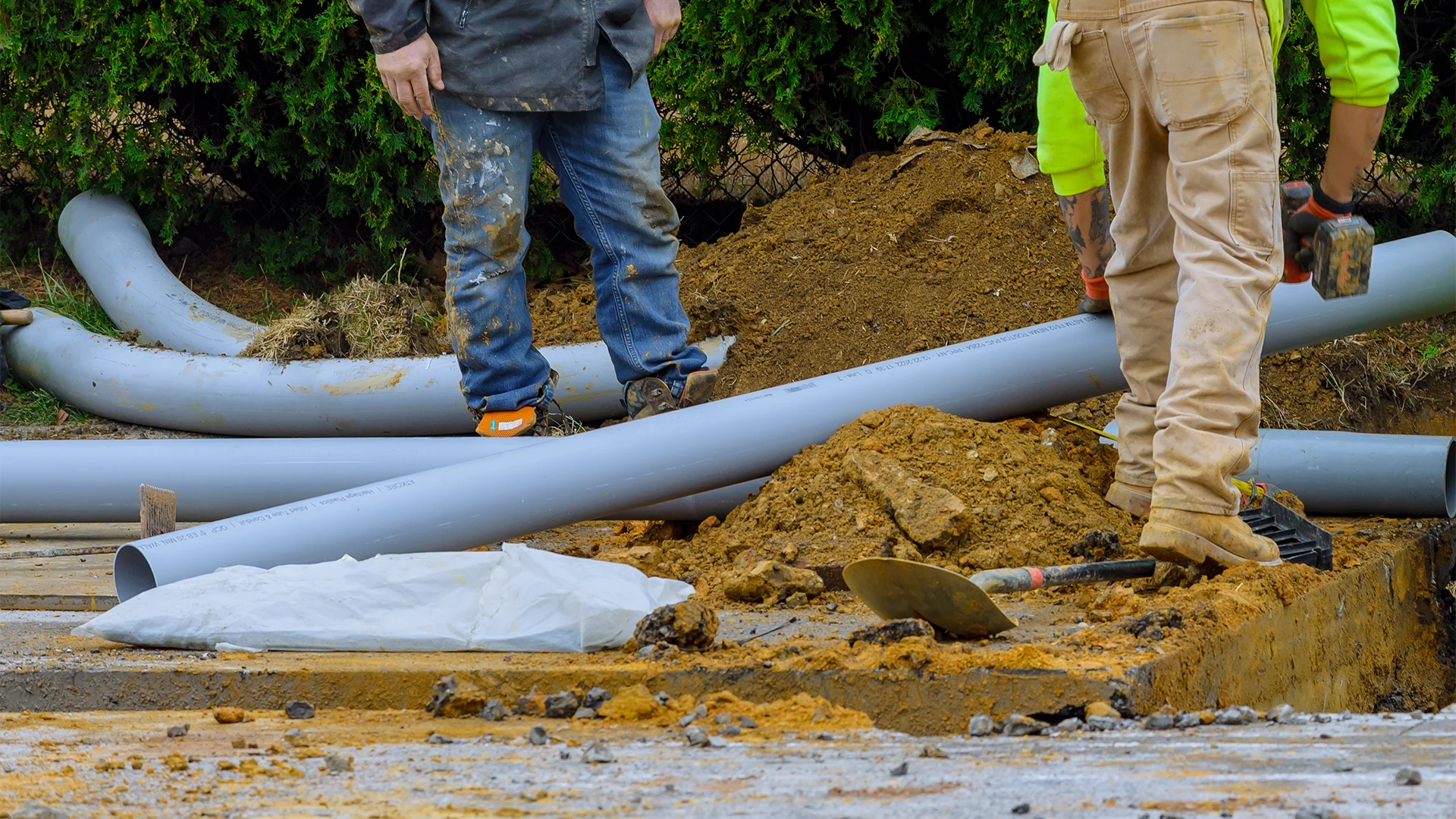 Construction workers installing large grey PVC underground utility pipes at a dirt excavation site